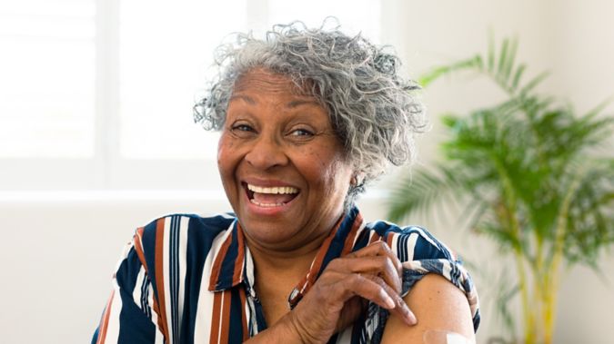 A woman grins and shows her bandaged arm. 