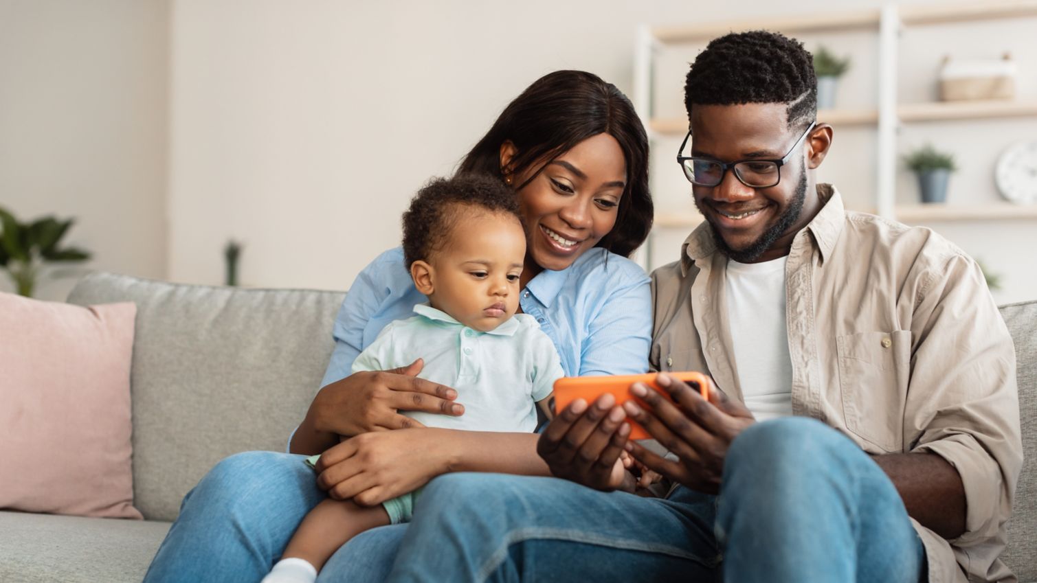 Happy young parents relaxing together on sofa using digital gadget, mobile phone