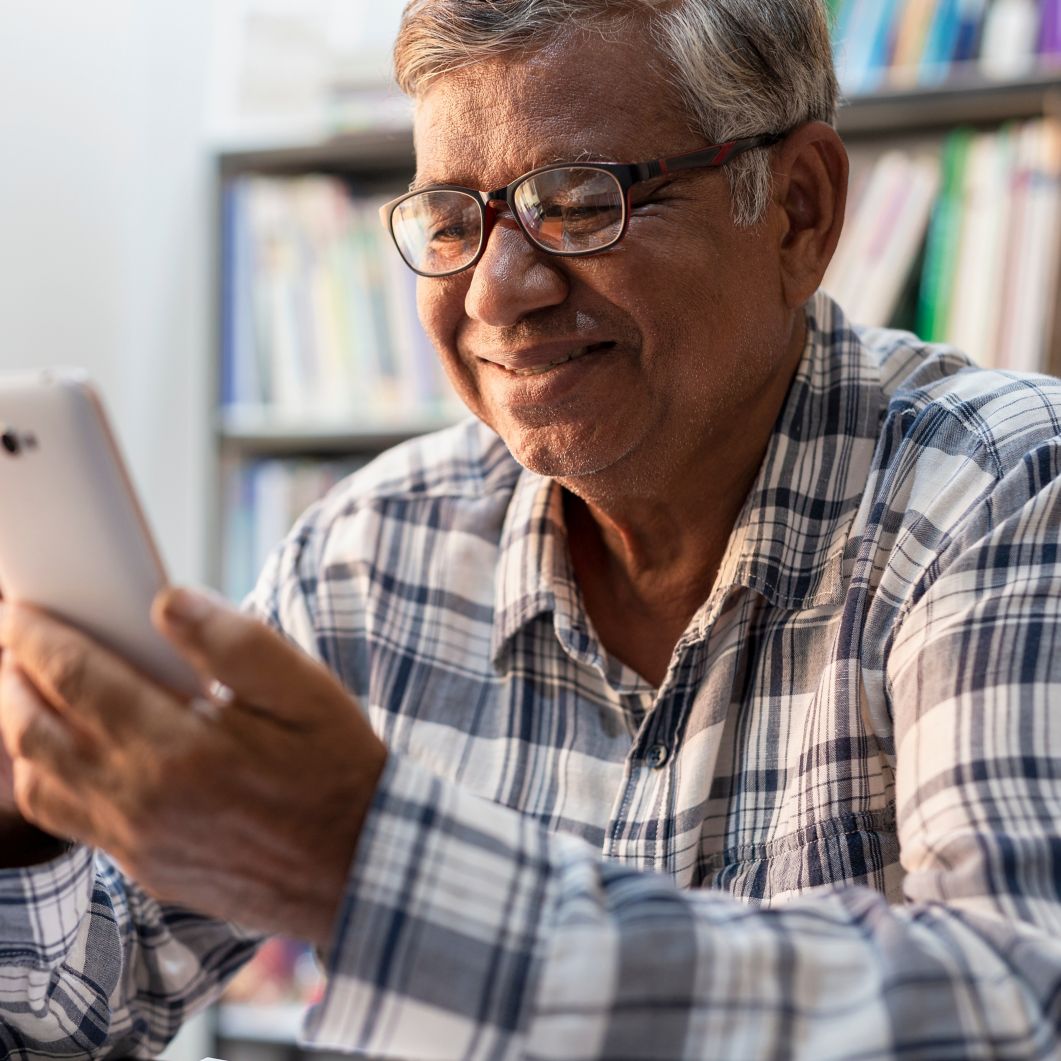 A man smiles while using a smartphone at home. 