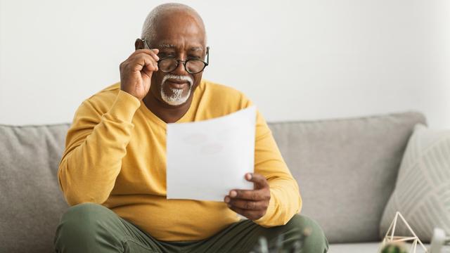 A man adjusts his glasses while reading on his sofa. 