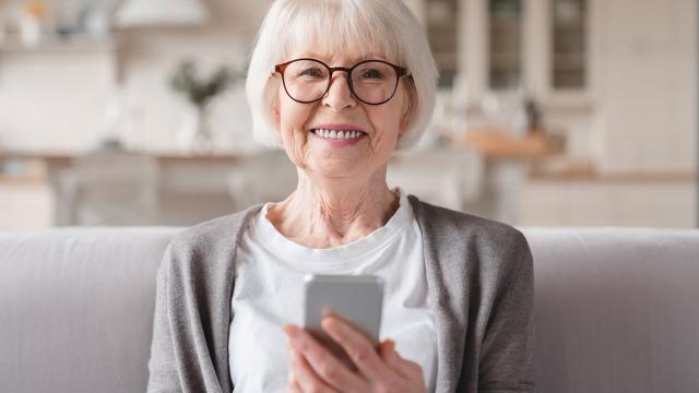 A woman smiles and holds a smartphone. 