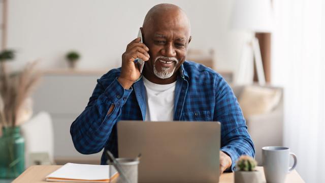 A man makes a phone call while looking at his computer. 