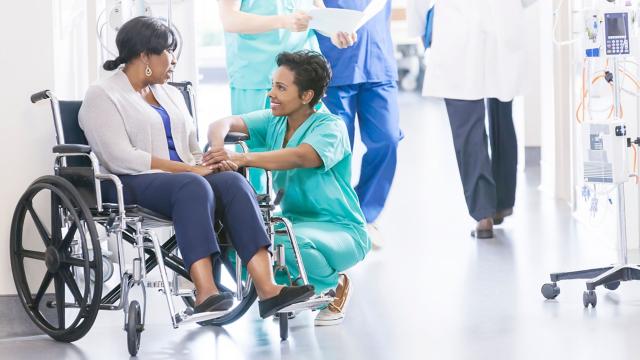 A woman in a wheelchair speaks with a nurse in a hospital. 