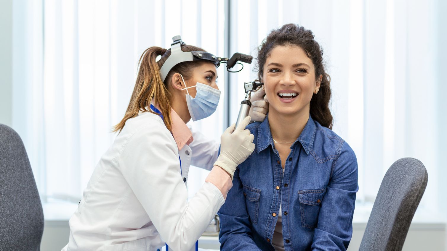 Hearing exam. Otolaryngologist doctor checking woman's ear using otoscope or auriscope at medical clinic. Otorhinolaryngologist pulling ear with hand and looking at it with otoscope closeup.