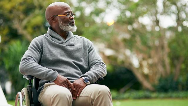 A man smiles at someone in the distance in his wheelchair at a park. 