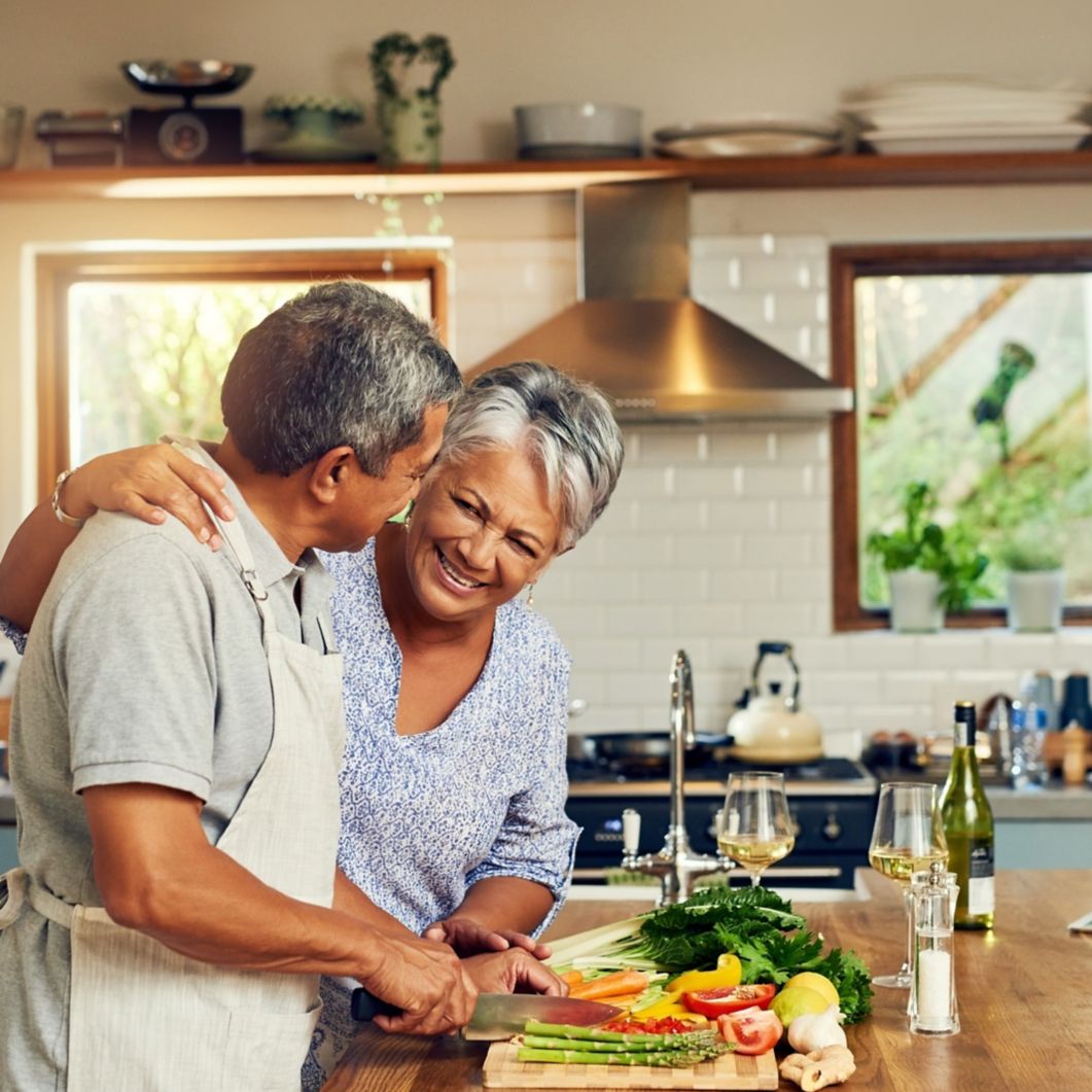 A woman smiles and she and her partner cook together. 