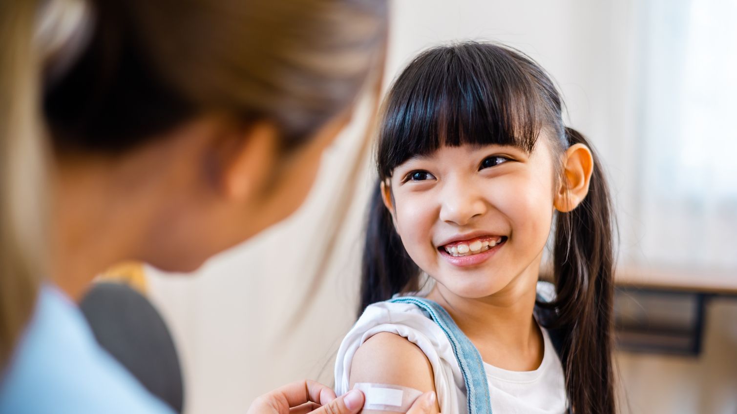 Healthcare provider places bandaid on smiling girl after flu shot.