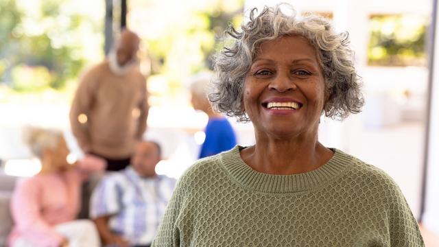 A woman smiles at the camera while her friends are seated behind her. 