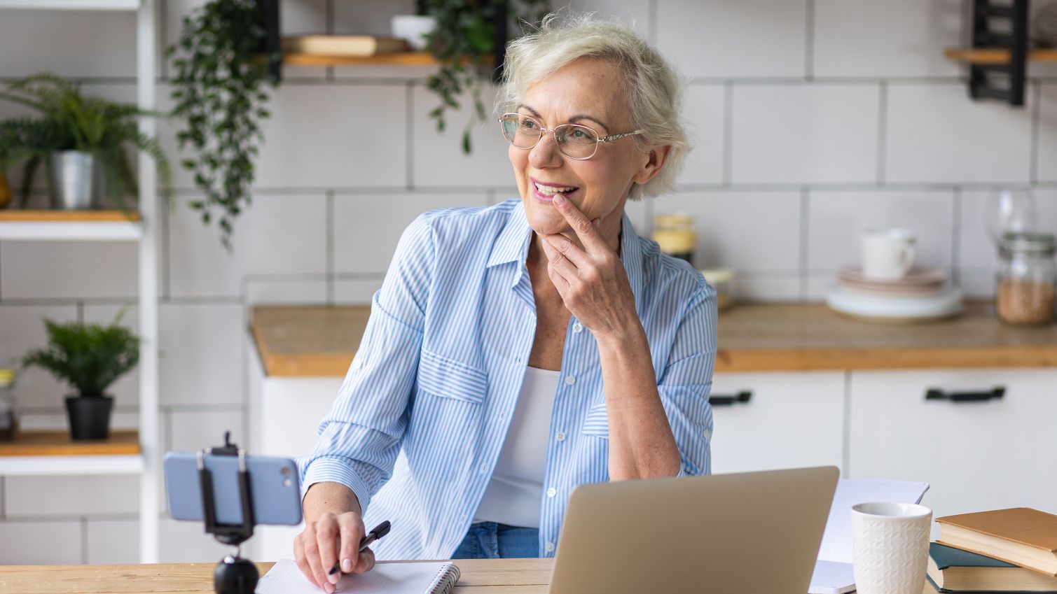 Senior-aged woman sitting at home office deck, smiling while on a virtual visit call. 