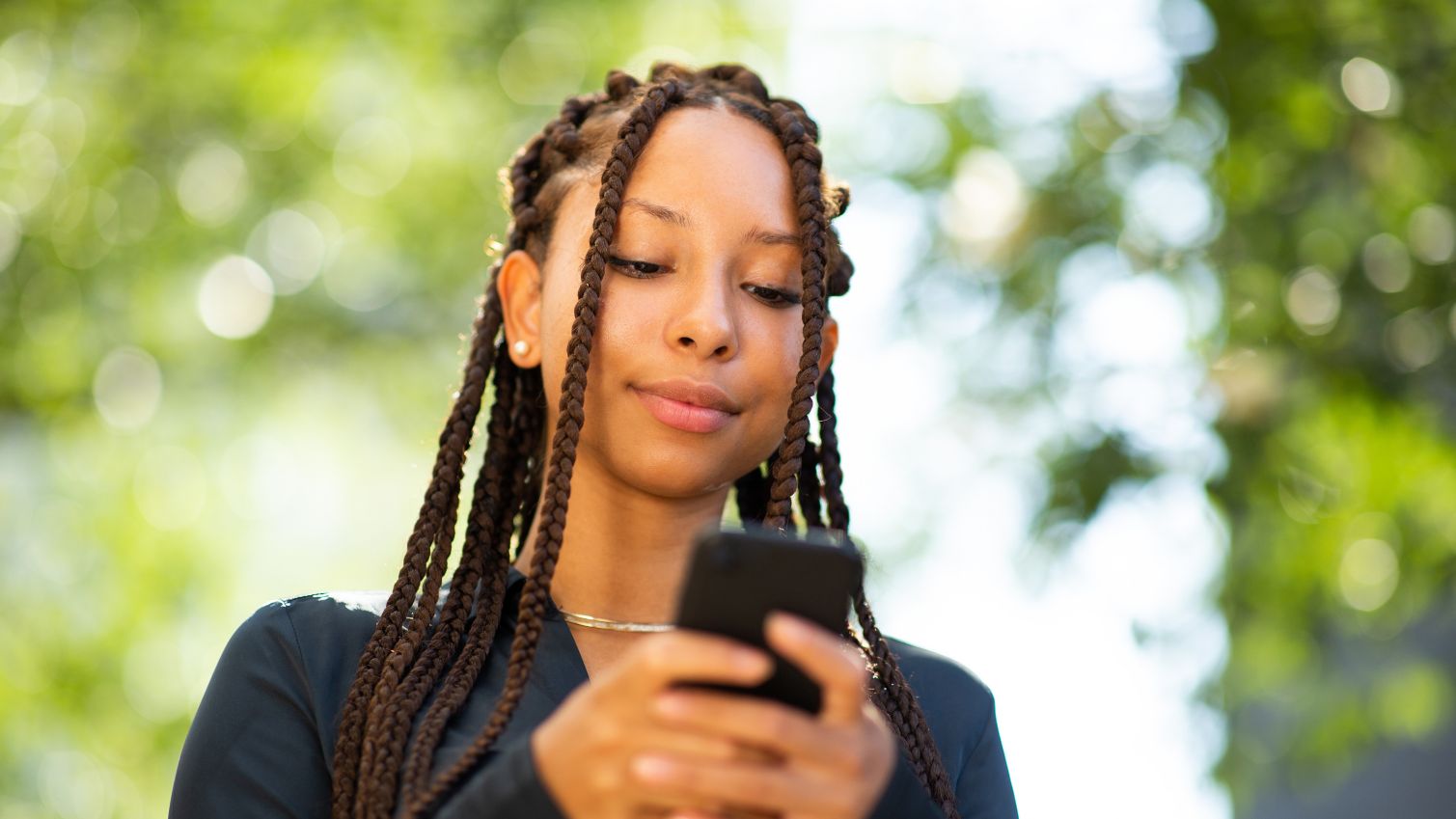 Young black woman texting with her smartphone outside in the city