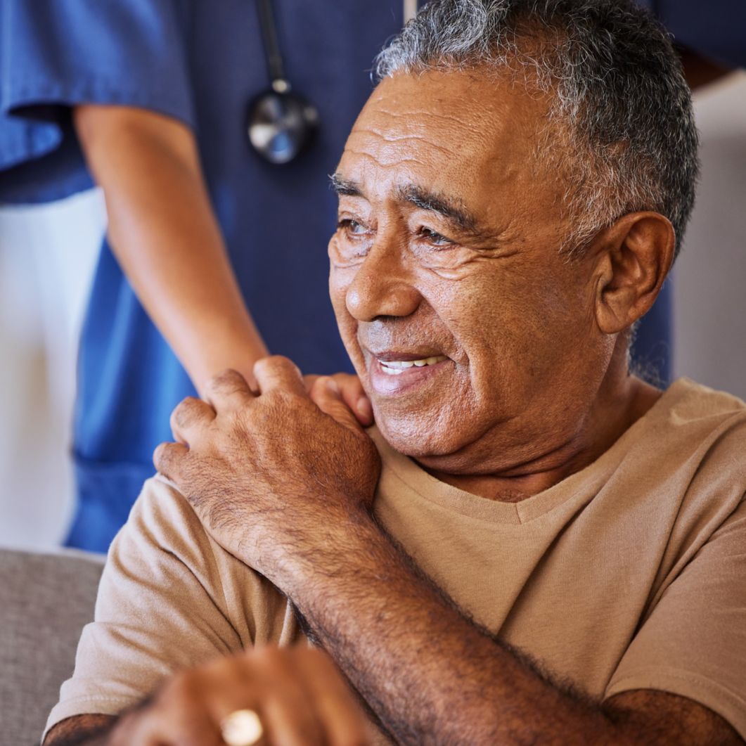 A nurse rests her hand on an older man's shoulder