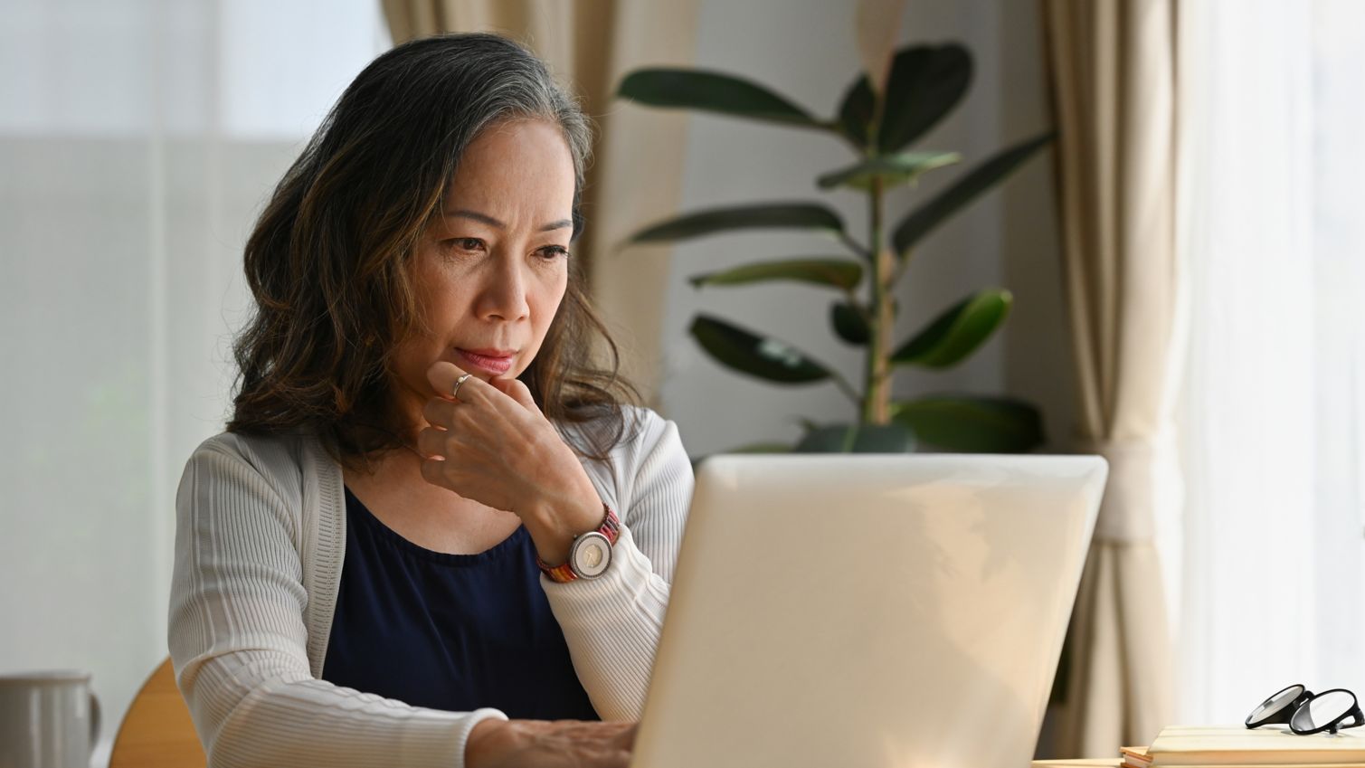 A woman sits in her home reading a laptop screen. 