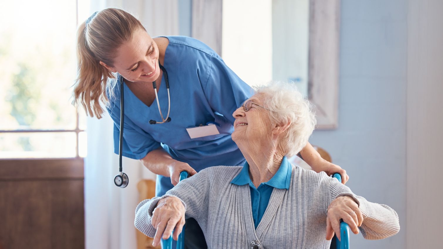 Patient smiles up at her care provider while being pushed in a wheelchair.