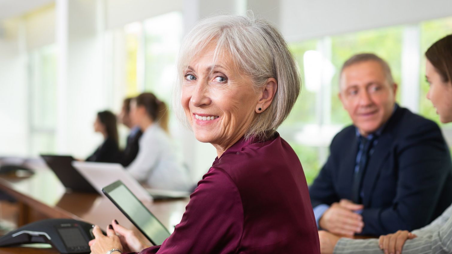 Woman at conference table smiles at camera.