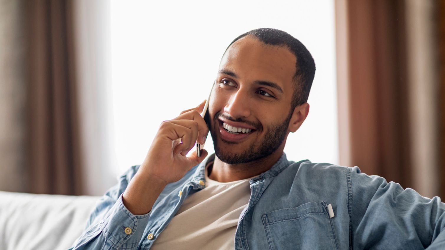 A man sitting on a couch talks on the phone.