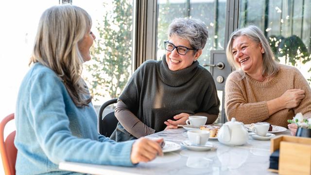 Three women laugh while having coffee together. 