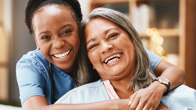 A woman smiles as her caregiver hugs her. 