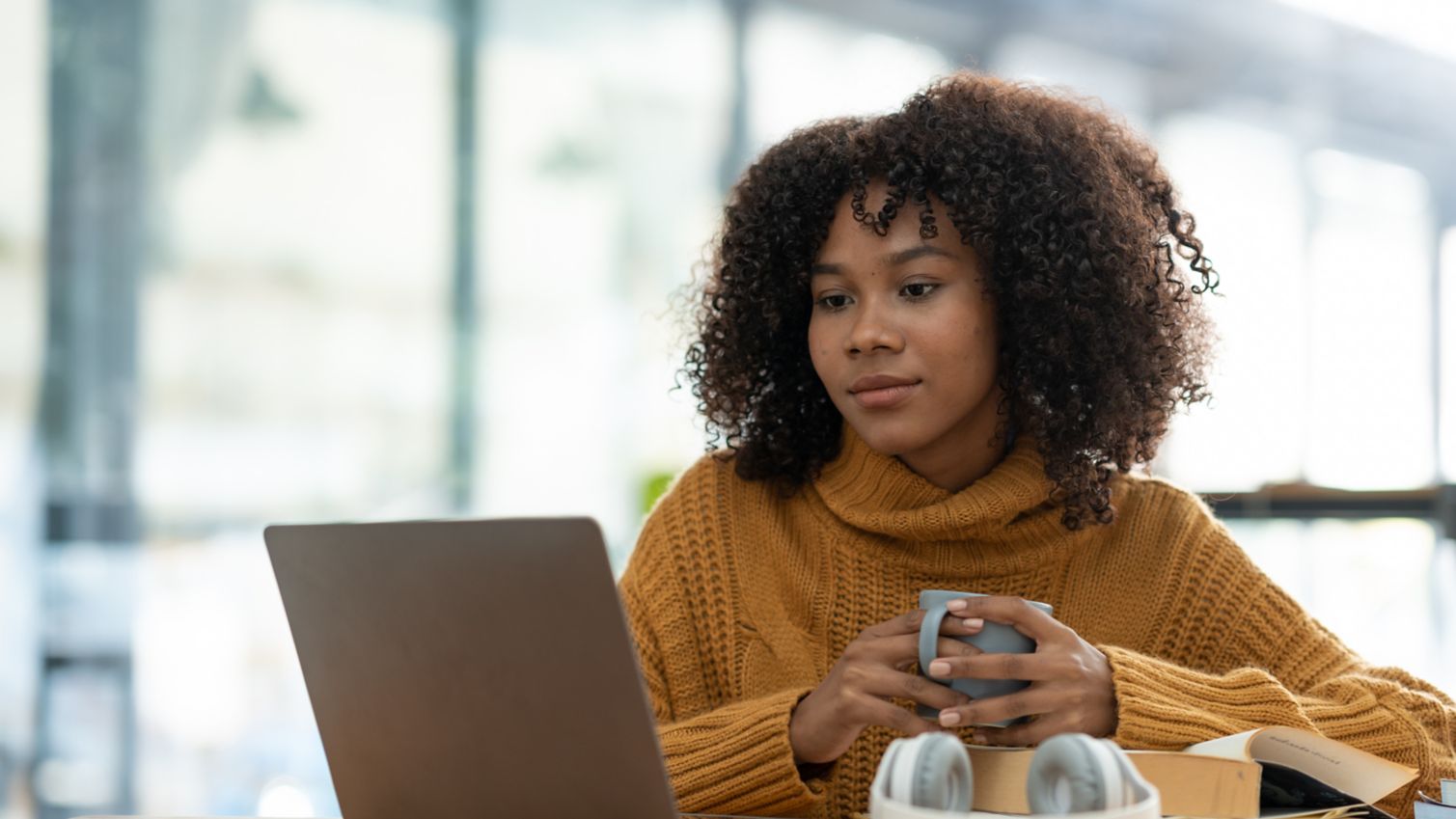 Woman drinks coffee while checking her phone and laptop