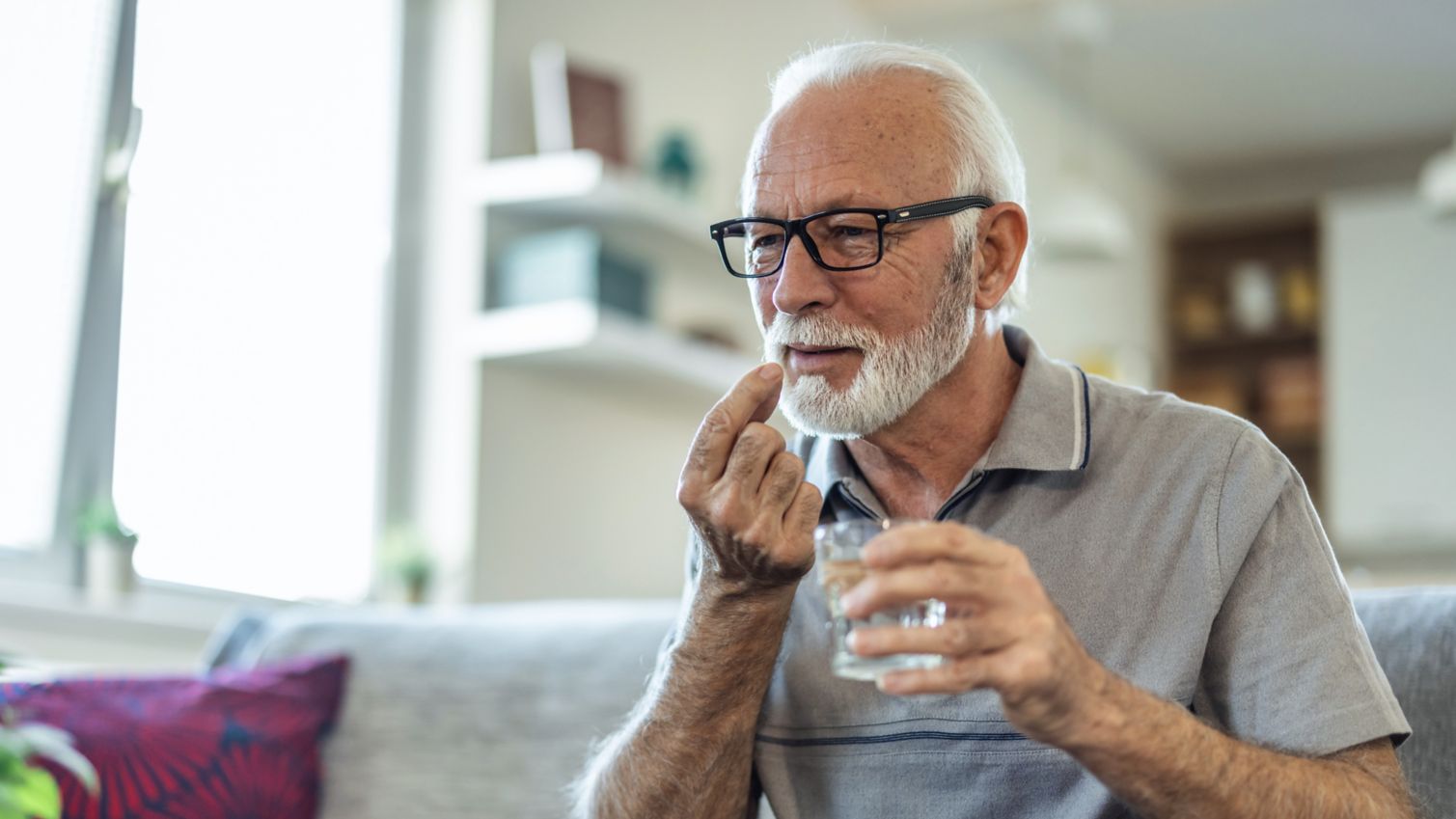 A man holds a glass of water and prepares to take his medicine. 