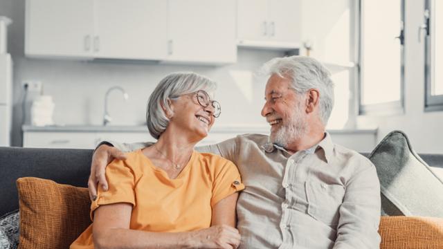 A couple relaxing on the couch at home share a hug and a laugh.  