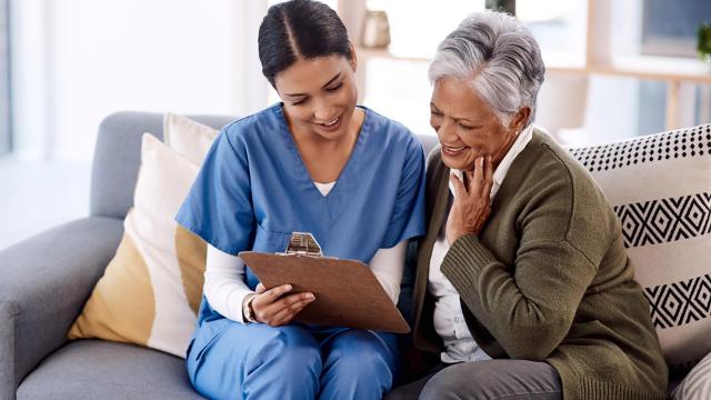 A woman looks at a clipboard her nurse is holding. 