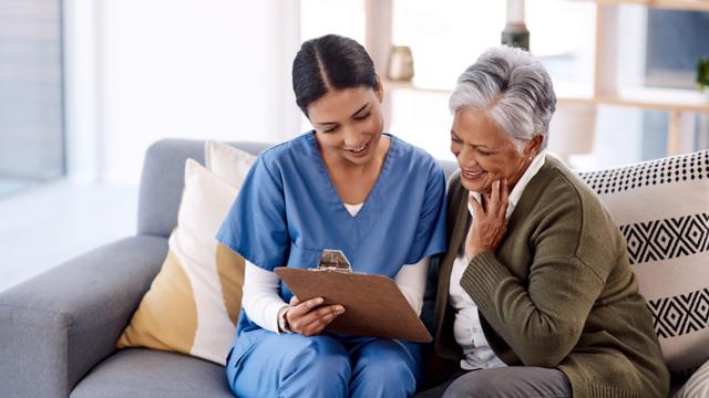 A woman looks at a clipboard her nurse is holding. 