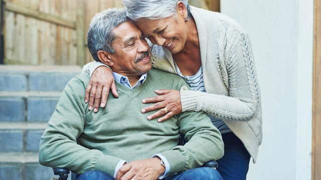 A man in a wheelchair is hugged by his wife. 