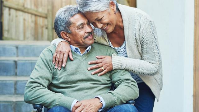 A man in a wheelchair is hugged by his wife. 