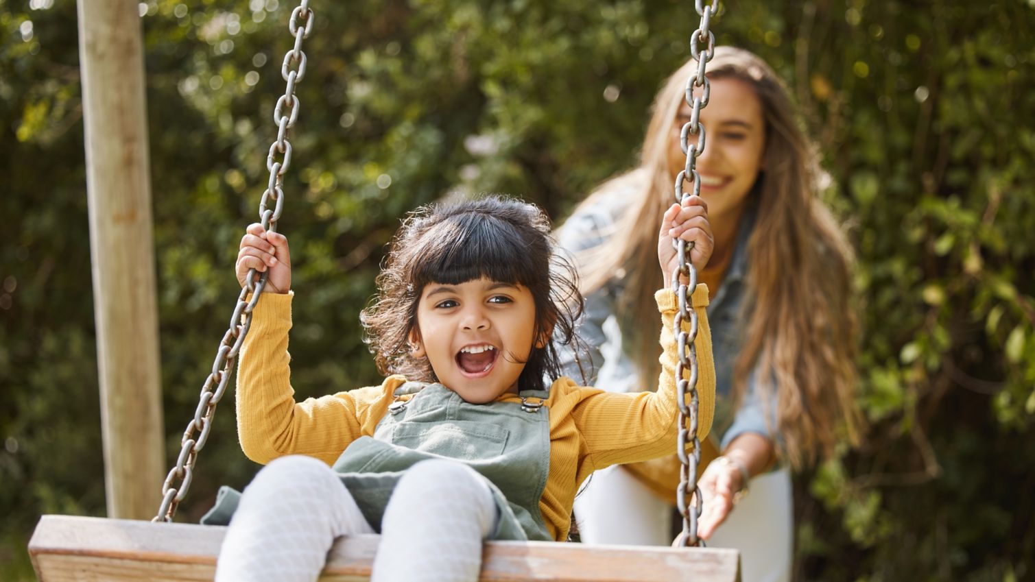 Child being pushed on a swing by an adult.