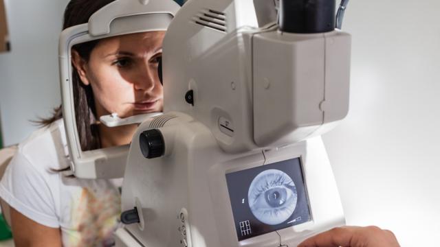 A woman looks into a retinal camera during an eye exam.