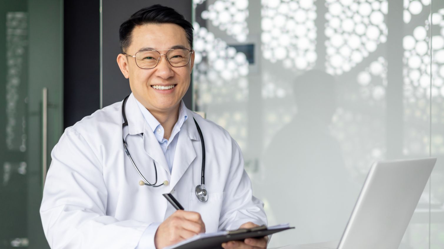 Doctor smiling in office with laptop.