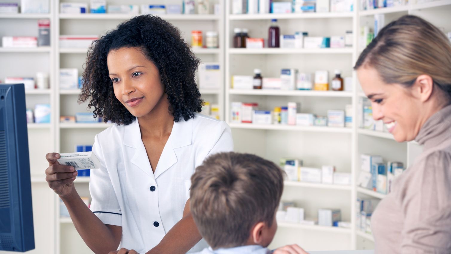 A doctor writes out a prescription at a pharmacy counter next to a girl sitting on the counter.