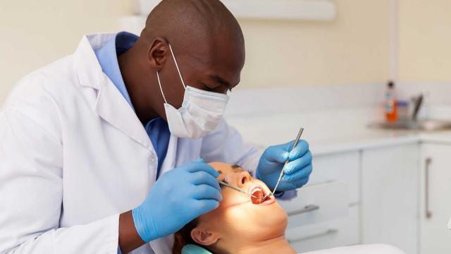 A dentist checks their patient’s teeth for cavities. 