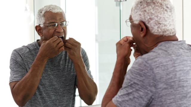 Senior man flossing teeth in mirror.
