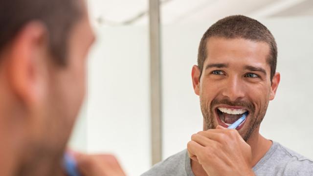 Man brushing teeth in mirror.