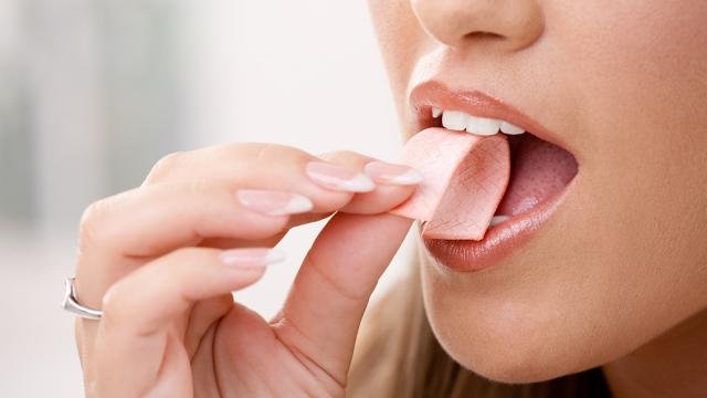 A woman puts a piece of chewing gum into her mouth. 