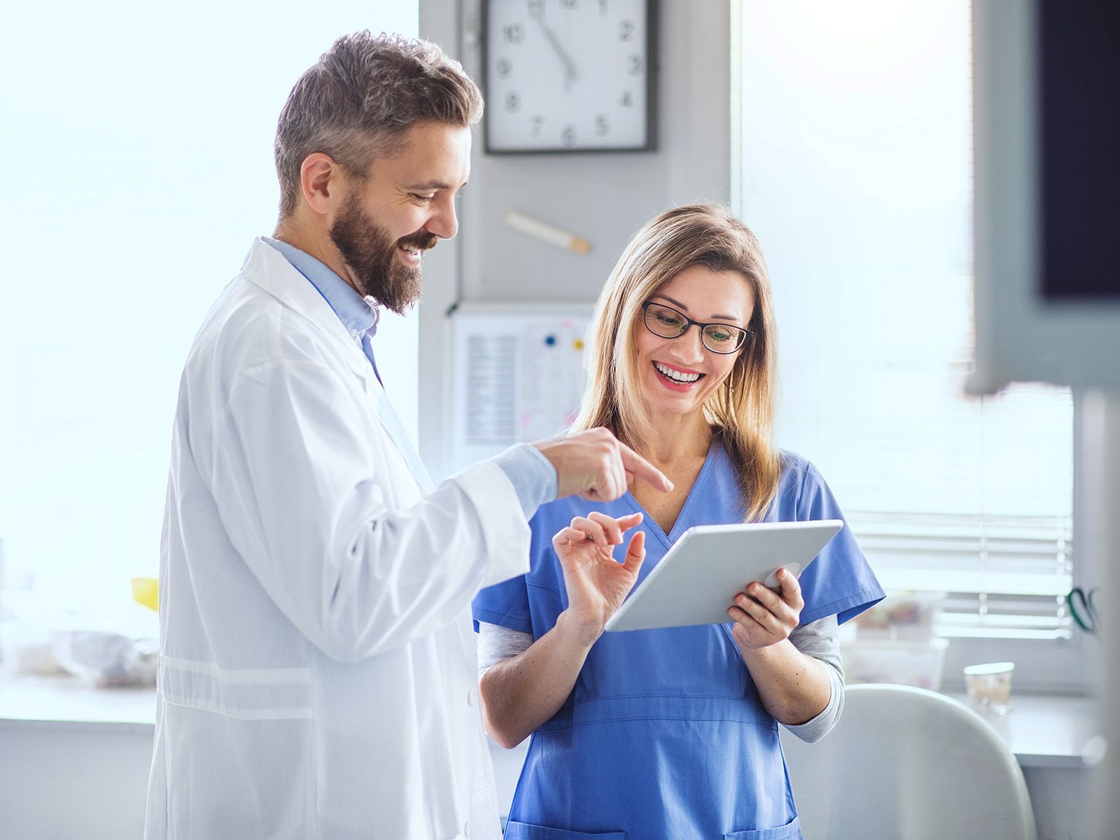 A dentist is having a friendly discussion with an assistant holding a tablet.