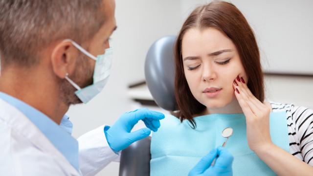 A woman holds her cheek as she speaks with an emergency dentist. 