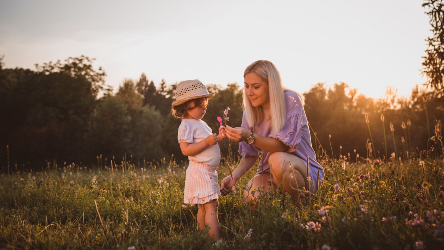 Mom picks wild flowers with young child in a field