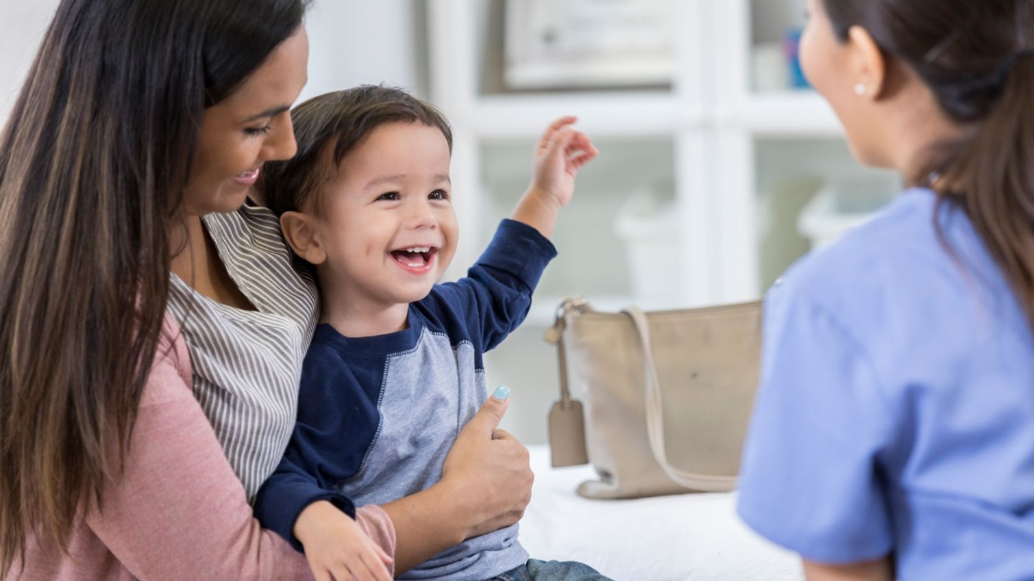 A mother and young boy laugh as they talk to a physician during a medical exam