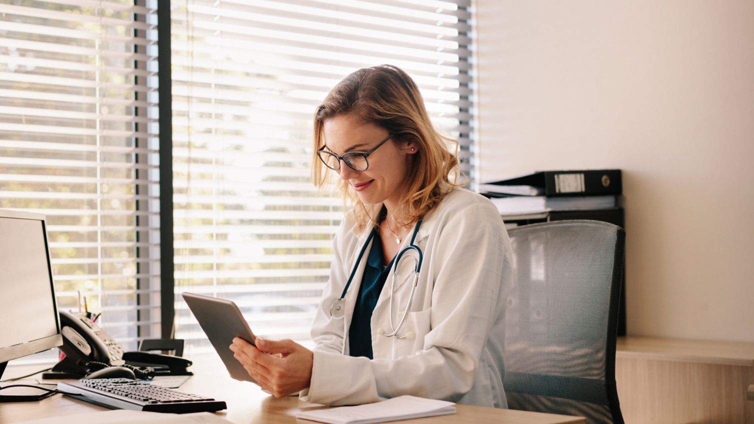 A smiling female doctor researches information on a tablet