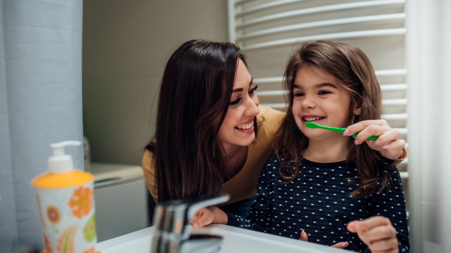 Mom helps her daughter brush her teeth