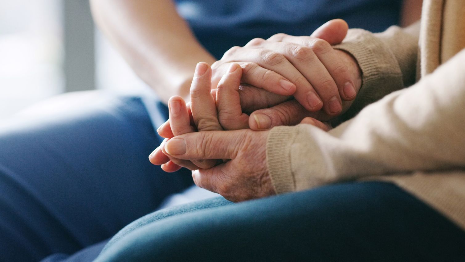 A healthcare professional and an elderly patient hold hands