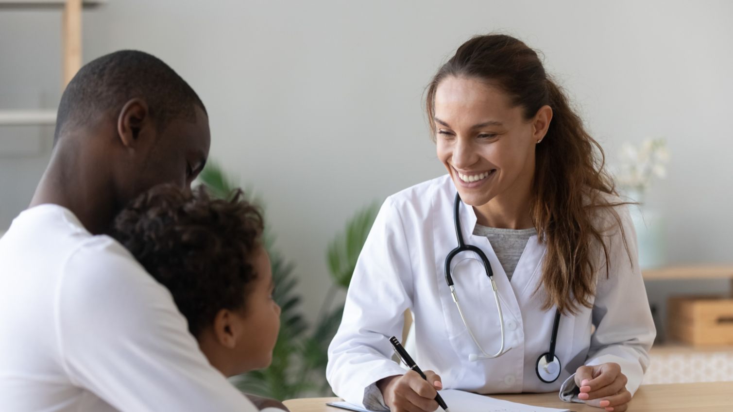 A female physician smiles while talking to a young child and his father