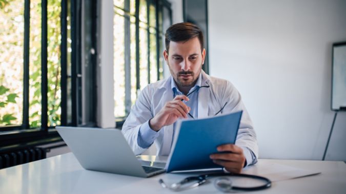 A male physician reviews a packet of information while sitting at his desk