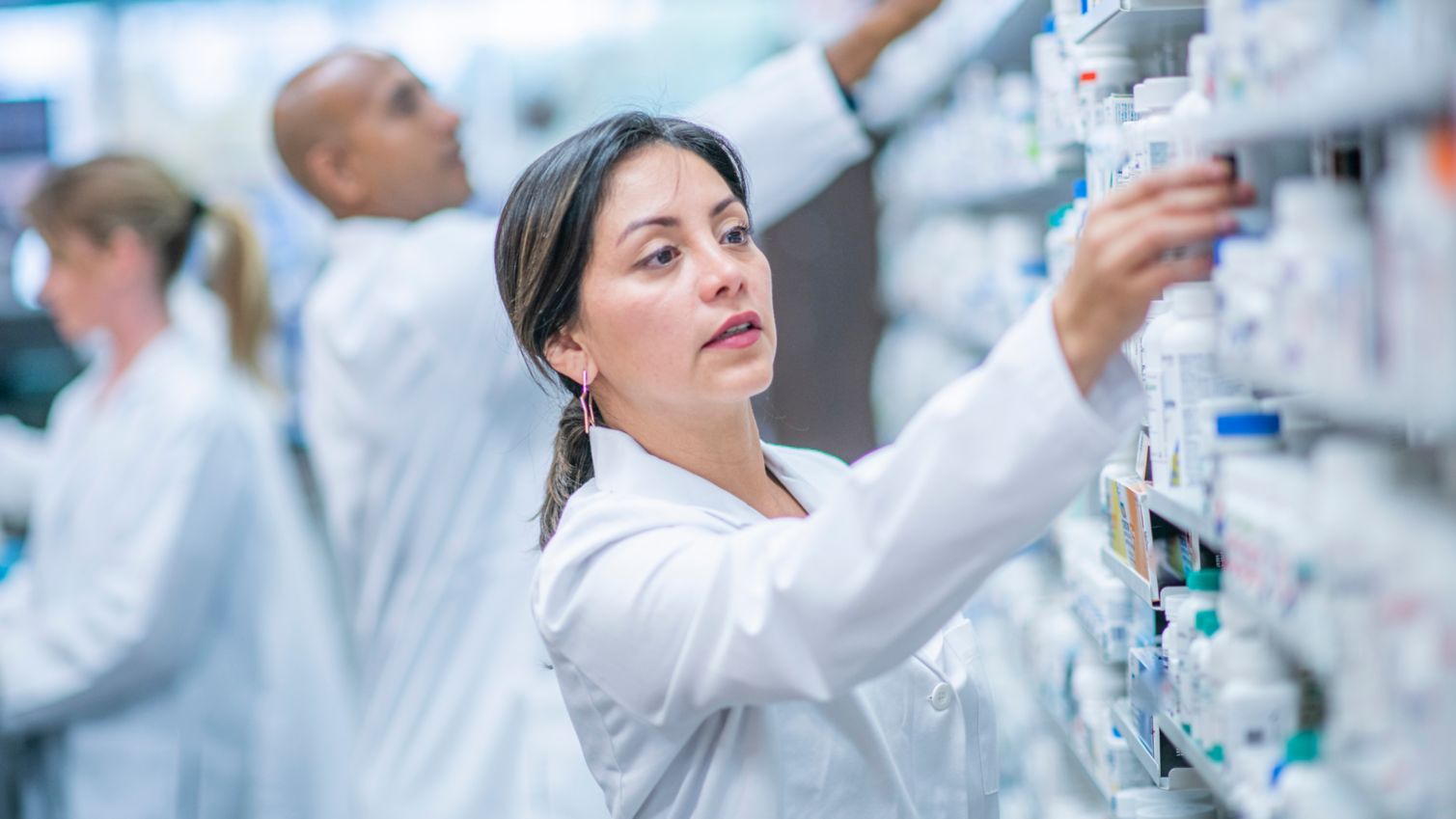 A female pharmacist choses a prescription drug from a shelf in the pharmacy