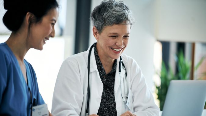 Two female healthcare workers research information on a laptop