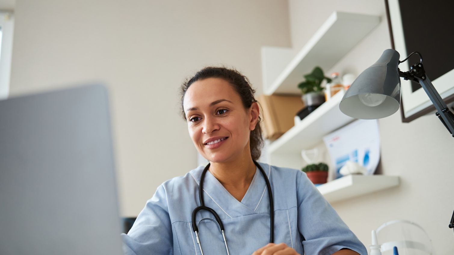 A smiling healthcare worker enters information on her laptop