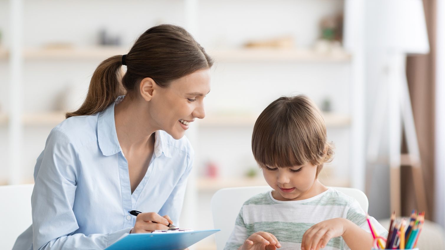 A behavioral health professional takes notes while a child plays at table