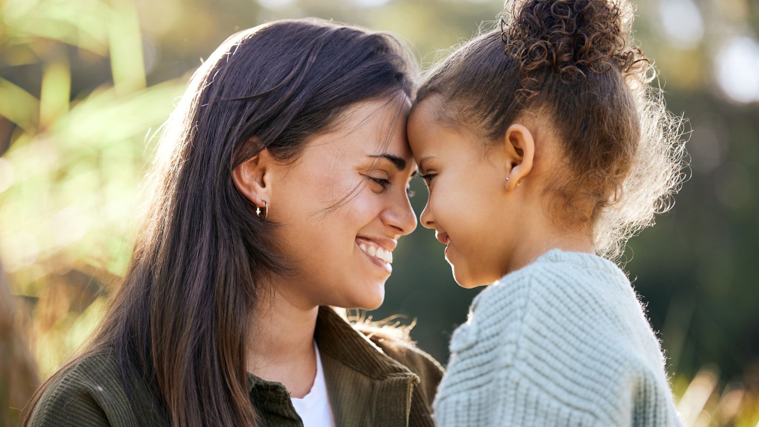 Mom holding daughter touching foreheads smiling while outside